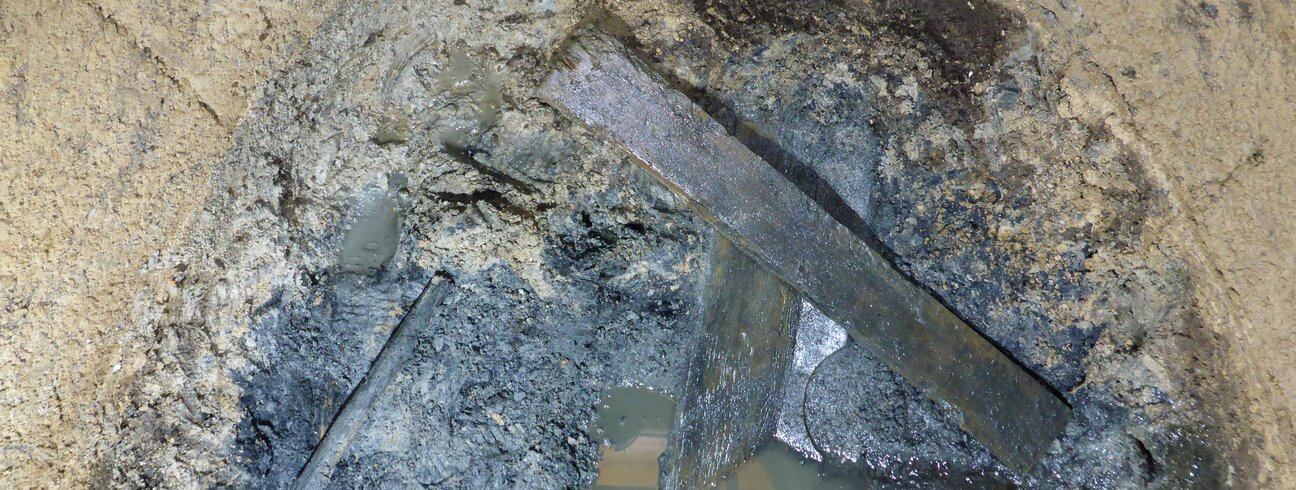 Soubor prken na povrchu fekálního sedimentu – pozůstatky dřevěné konstrukce latrín. Soubor prken na povrchu fekálního sedimentu – pozůstatky dřevěné konstrukce latrín.